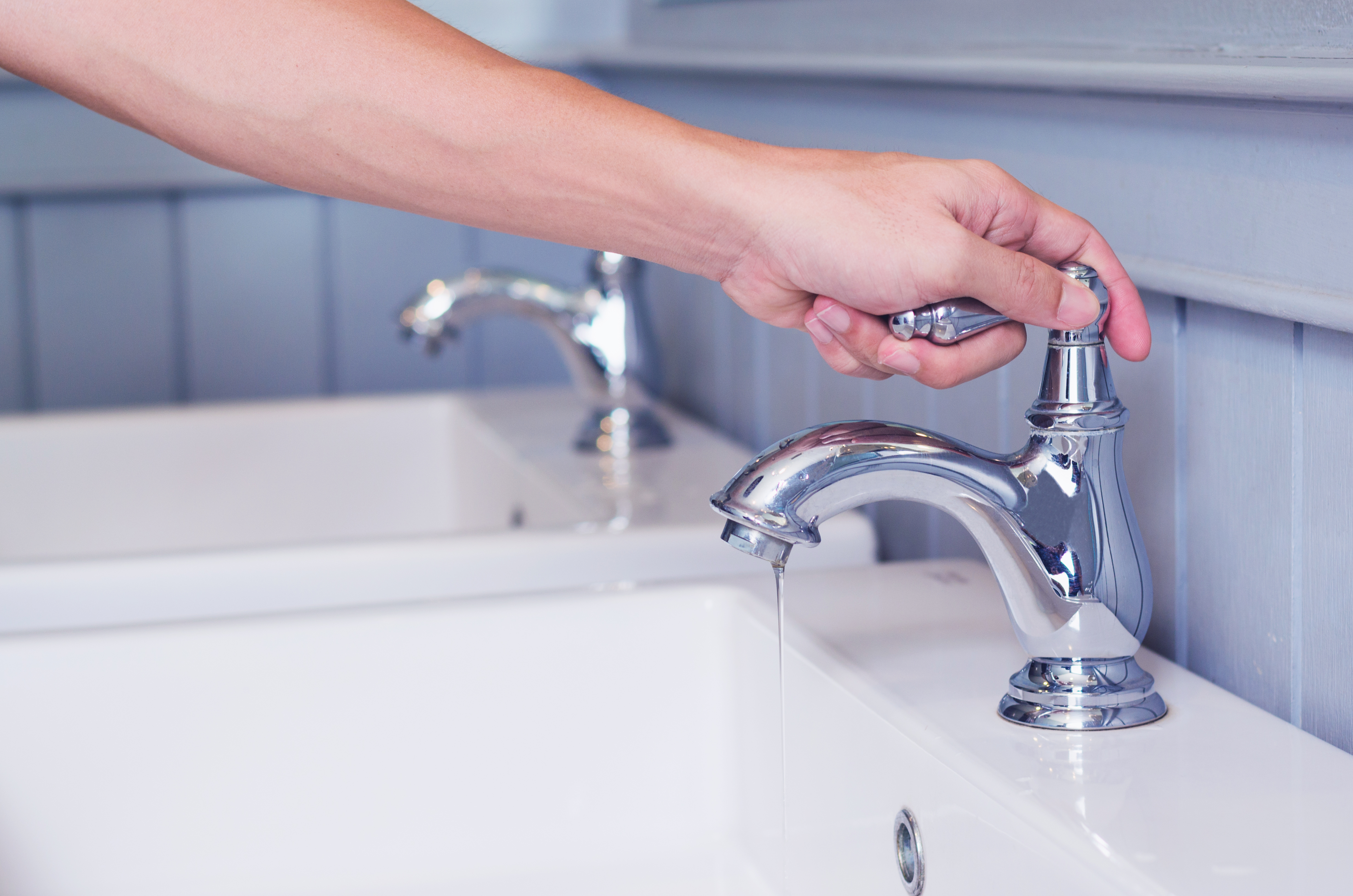 hand man opening silver faucet or water tap with white washing sink in public toilet. - Plumbing Services